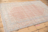 A low-angle view of a vintage Persian rug's repeating boteh pattern in blush and ivory.