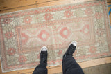 Standing view of a distressed Oushak runner's low pile and soft ruby red and silver geometric design.