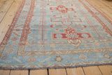 Distressed vintage Malayer rug bottom edge showing powder blue field, simplistic florals, and fringe.