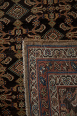 Folded corner of an antique Hamadan showing the dark pile, woven back, and intact side selvage.