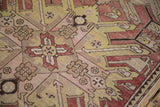 Detail of a distressed Kazak rug showing even wear on starburst motifs in terracotta, yellow, and beige.