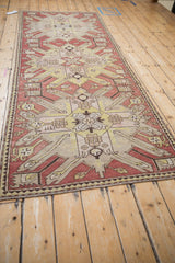 Perspective view of an antique Kazak runner's bold starburst medallions in terracotta and yellow.