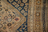Detail of a vintage Qashqai carpet's geometric diamond motifs and borders in navy blue, bronze, and ivory.