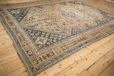 Corner detail of a distressed Qashqai carpet highlighting geometric borders in bronze and navy blue.