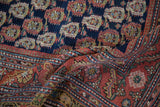Close-up of a folded antique Malayer rug with its navy boteh field and multi-tiered red floral border.