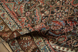 A folded view of an antique Persian rug showing the dense texture and colorful, intricate Herati pattern.