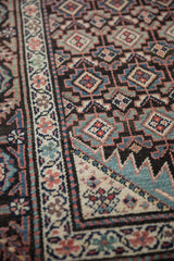 Angled detail of the intricate geometric guls and floral border on a low-pile antique Malayer rug.