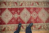 A view from above showing the distressed pile and dusty cherry red diamond pattern of an Oushak runner.