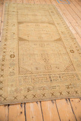 Geometric checkered corner motif and distressed cream pile texture on the vintage Oushak runner.
