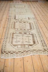 Distressed vintage Oushak runner featuring repeating beige, brown geometric guls and vine border.