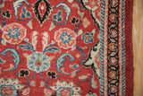 Scrolled serrated leaves and floral blossoms in blue and ivory on a brick red Persian rug.