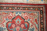 Corner of a vintage Arak rug with a meandering vine border, scalloped field, and ivory fringe.