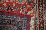 Folded corner of a vintage Arak rug showing its hand-knotted back, red selvage, and fringe.