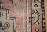 Distressed vintage Oushak rug detail with mauve and sand stepped spandrel, brown meandering plant border.