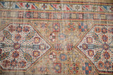 Antique Serab rug close-up: geometric hexagonal medallions, pinwheel florals, camel, blue, red hues, and foundation wear.
