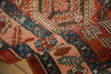 Rolled corner of an antique Heriz runner showing its textured, low pile and serrated leaf border.