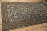 Angled view of a distressed Hamadan rug's corner spandrel and meandering vine borders.