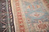 A distressed Karaja rug's geometric border contrasts with a dark traditional Persian rug.
