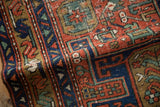 Close-up of antique Heriz rug's geometric motifs, brick red, navy, with mostly even wear.