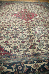 Angled view of a vintage Khorassan carpet showing its navy border and ivory field with Herati motif.