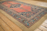 Antique Hamadan runner from an angle, displaying its diamond medallion on an abrashed red ground.
