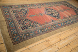 Angled view of an antique Hamadan runner with an abrashed ruby field and geometric diamond medallion.