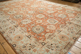 Angled view of a distressed Tabriz carpet's terracotta palmette field and pale powder blue border.
