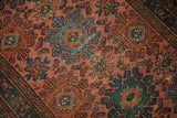 Mehriban rug detail: pale raspberry field, dusty teal hook-and-latch motifs, Mahi leaves, visible wear.