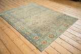 Angled view of a distressed Malayer rug with intricate cartouche medallions in dusty teal and copper.