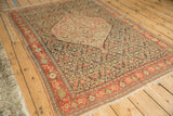 Angled view of antique Senneh rug's hexagonal medallion, charcoal Herati field, and ruby red border.