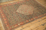 Angled view of an antique Senneh rug featuring its large hexagonal medallion and dark field.