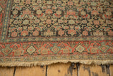 The end of an antique Senneh rug, detailing the worn pile, patterned border, and short fringe.
