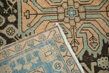 Folded corner of a distressed Hamadan rug reveals its hand-knotted foundation and low pile.