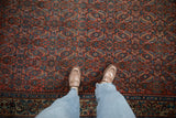 Vintage Bijar carpet's Herati motif in brick red, dusty blue, and rose tones, with loafers.