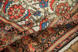 Folded vintage Malayer rug, revealing Herati pattern detail on ivory ground with red and blue.
