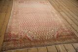 Angled view of a vintage distressed Malayer rug, highlighting the field of staggered blossoms and warm palette.
