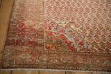 Corner view of the distressed Malayer rug's pomegranate spandrel in tangerine and cherry red.