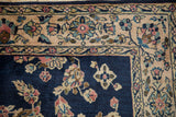 Corner close-up of a vintage Sarouk rug's platinum rose border and floral navy blue field.