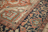 Close-up of antique Serapi carpet: navy border floral vines, brick red field with even pile.