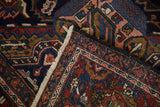 Folded vintage Heriz carpet corner showing cherry red, navy, gold Herati motifs and fringe.