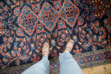 Vintage Lilihan carpet's traditional pattern in sapphire blue and red, shown for scale underfoot.