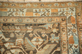Corner of a distressed vintage Malayer rug showing geometric borders in tangerine, brown, and sky blue.