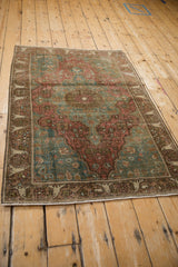 Corner of distressed Farahan Sarouk rug, faded red and green floral pattern with visible wear.