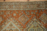 Distressed vintage Heriz rug close-up, showing worn pile texture and muted terracotta and green motifs.