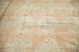 Distressed vintage Kashan carpet showing softened beige and rose tones with ornate cloudband panels.