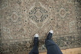 Feet on a distressed vintage Karaja rug, highlighting its muted beige and charcoal tribal patterns.