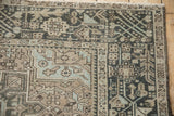 Corner of distressed Karaja rug with geometric patterns, worn pile, muted charcoal, beige, and blue.