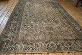 Angled perspective of a distressed Persian carpet showcasing its intricate geometric pattern in neutral, earthy tones.