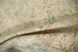 A soft fold in a distressed vintage rug highlighting its worn texture in beige, sky blue, and coffee tones.