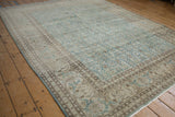 Angled view of a distressed Tabriz carpet's detailed Herati border and dusty ocean blue field.